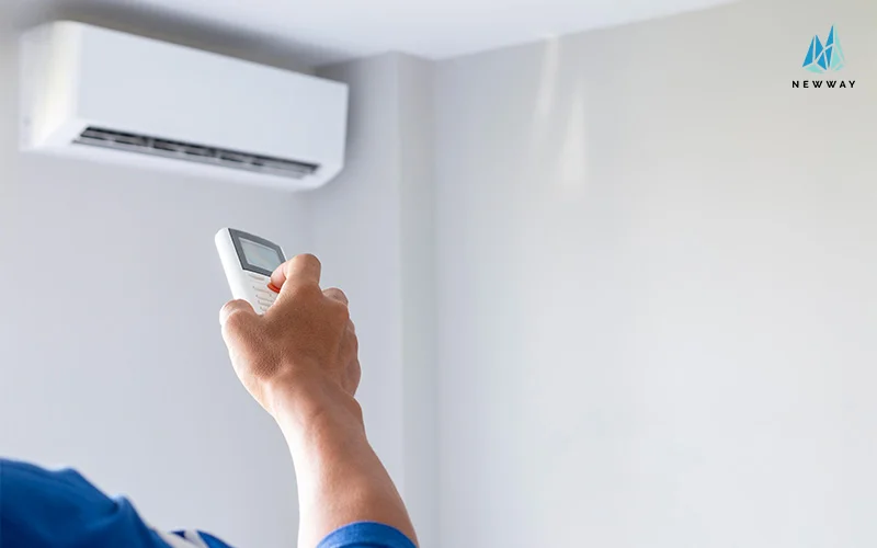 Hand holding remote towards mounted air conditioner.