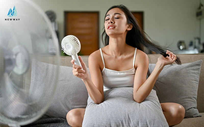 Woman cooling off with fan on couch.